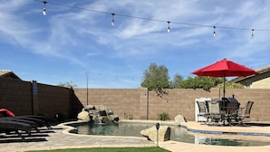 A backyard with a swimming pool, patio furniture, and string lights. - Young Desert Oasis with Heated Pool in Estrella Mountain Ranch (Goodyear)
