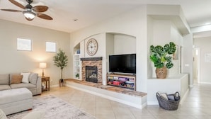 A living room with a fireplace, a television, and a ceiling fan. - Young Desert Oasis with Heated Pool in Estrella Mountain Ranch (Goodyear)