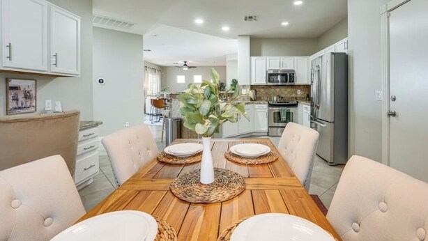A dining area with a wooden table, white chairs, and a vase with green plants. - Young Desert Oasis with Heated Pool in Estrella Mountain Ranch (Goodyear)