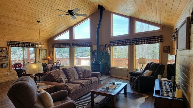 A cozy cabin interior with a wooden ceiling, large windows, a fireplace, and a dining area. - Welcome to Duck Creek Haven A fully furnished cabin secluded in a serene setting (Duck Creek Village)