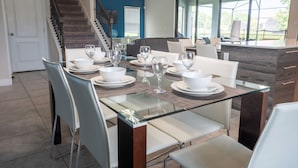 Un espace repas moderne avec une table à plateau en verre, des chaises blanches et un escalier en arrière-plan.