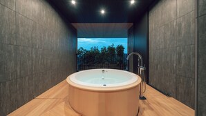 A modern bathroom with a wooden bathtub, dark tiled walls, and a view of trees through a large window. - Hotel Vison (Taki)