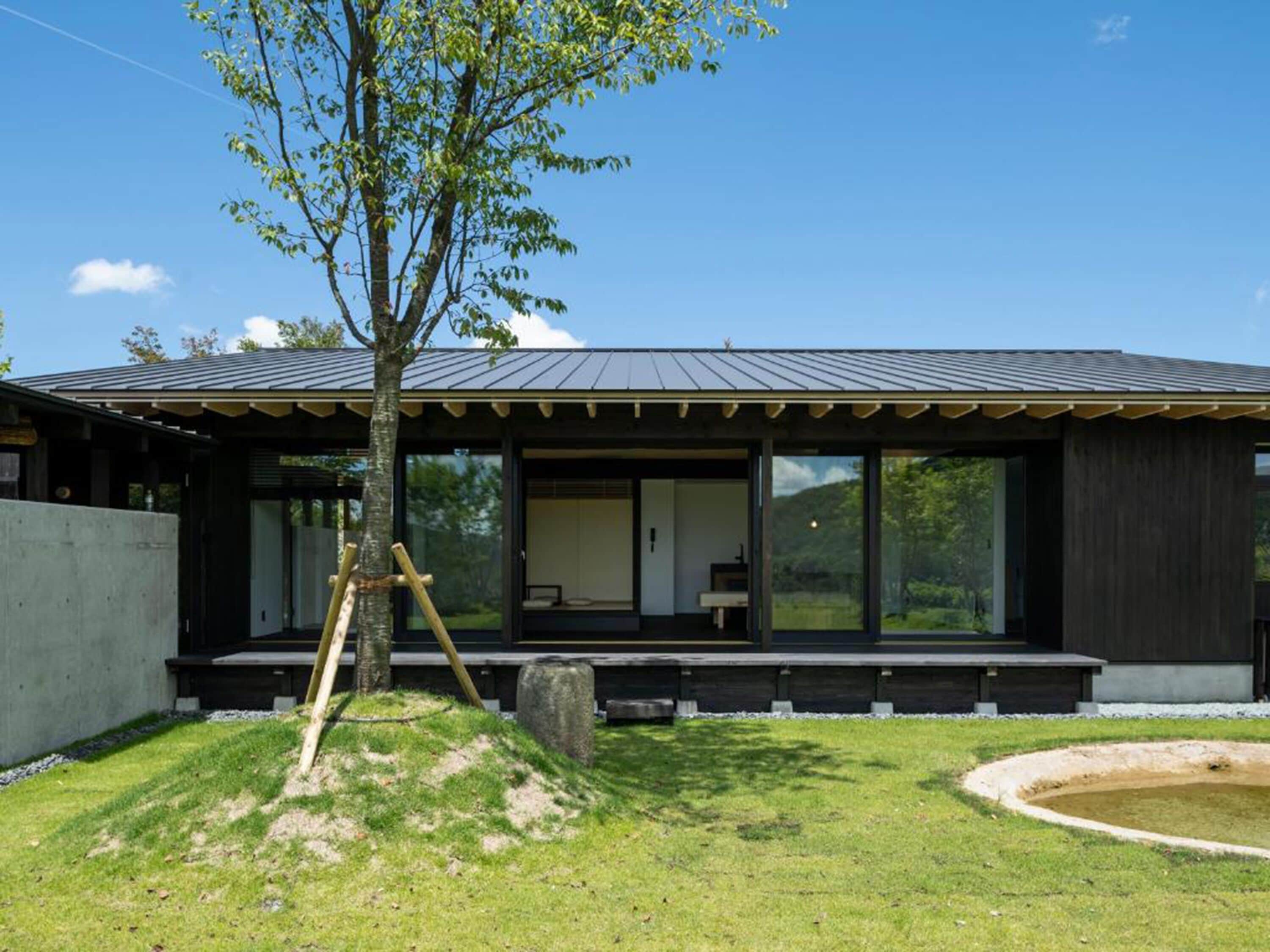 A modern house with a large glass window, a wooden deck, and a small pond.
