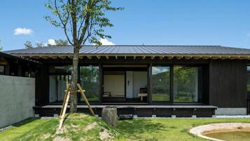 A modern house with a large glass window, a wooden deck, and a small pond.