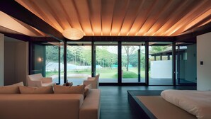 A modern interior with a wooden ceiling, a sofa, a bed, and large glass doors leading to a garden. - Hotel Vison (Taki)