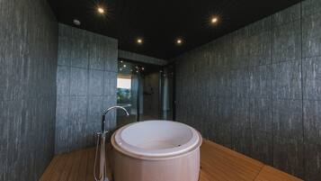 A modern bathroom with a freestanding bathtub, wooden flooring, and dark stone walls.