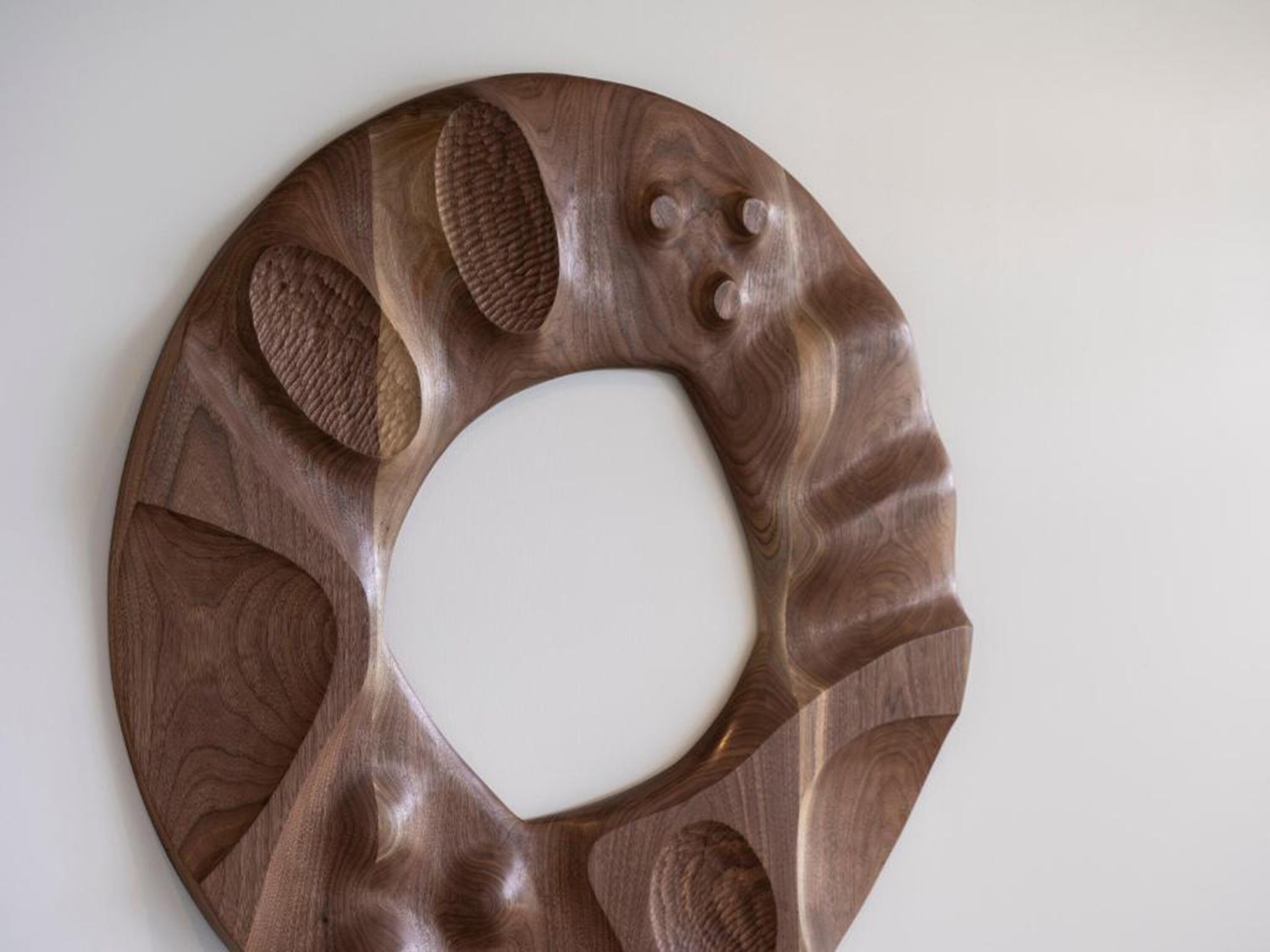 Une œuvre d’art murale circulaire en bois, ornée d’un trou central et de divers motifs et textures sculptés.