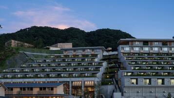A modern hotel with multiple floors, outdoor terraces, and a view of a forested hill.