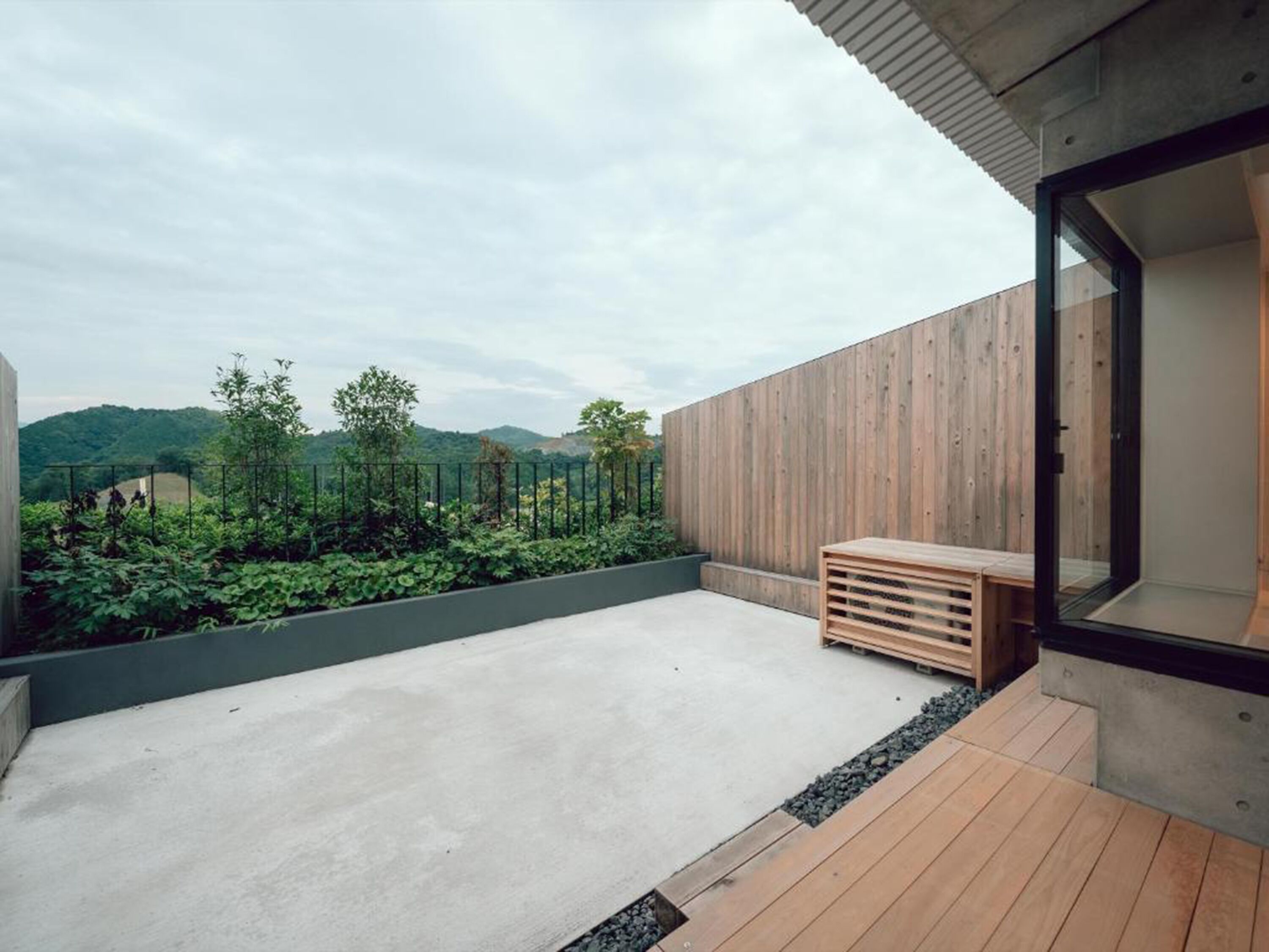 A modern outdoor space with a concrete floor, wooden deck, and a view of a green landscape with hills.
