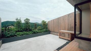 A modern outdoor space with a concrete floor, wooden deck, and a view of a green landscape with hills.