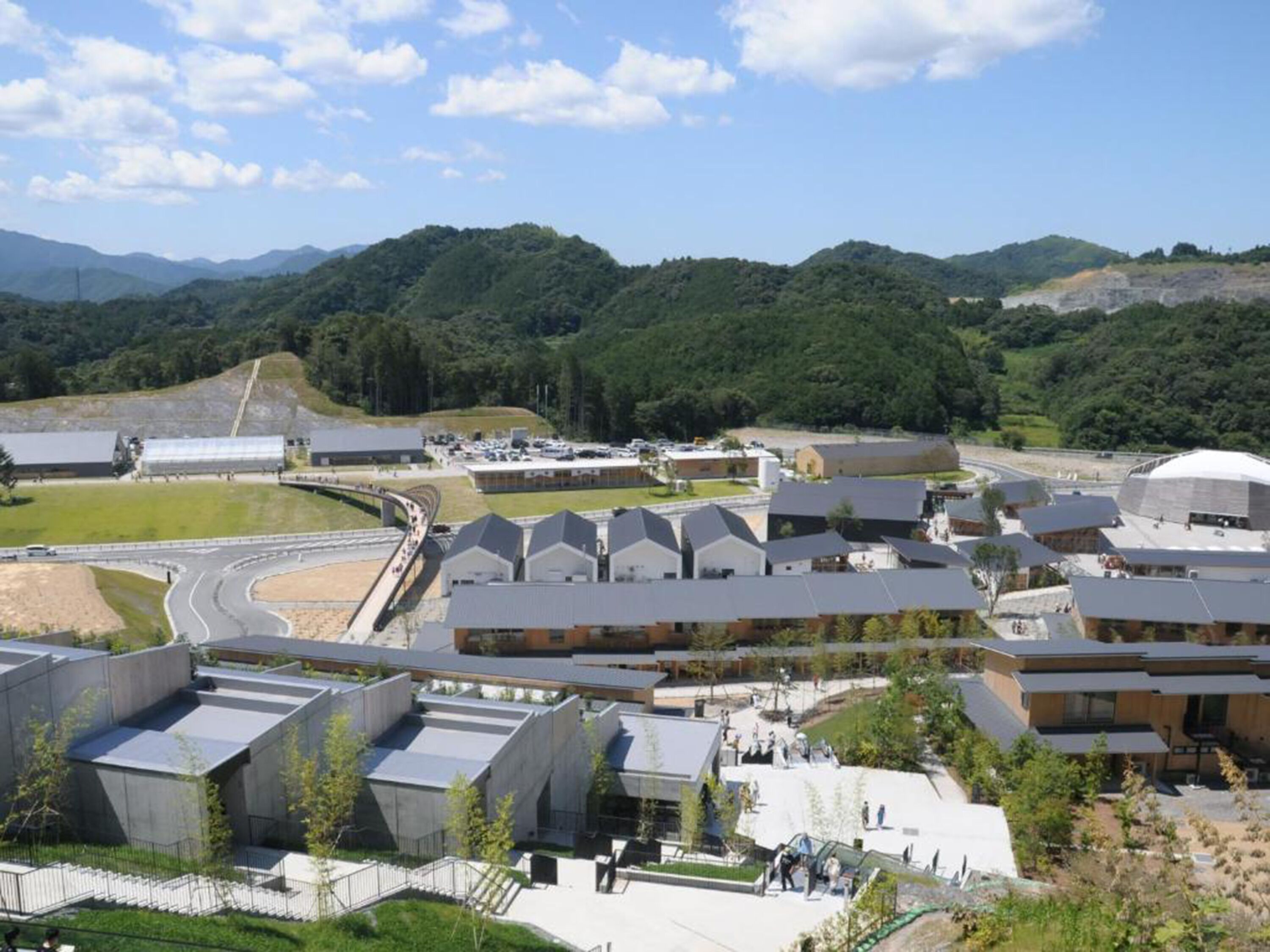 Un moderno complejo arquitectónico con varias construcciones, incluyendo una cúpula grande y varios edificios rectangulares, rodeado de zonas ajardinadas con una carretera que lo bordea.