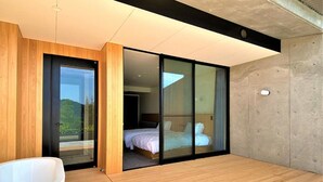 A modern bedroom with a large sliding glass door leading to a balcony, a wooden floor, and a white bathtub. - Hotel Vison (Taki)