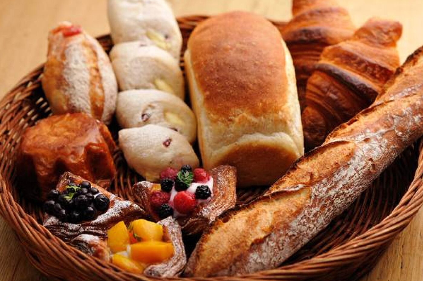 Ein Korb mit verschiedenen Brotsorten und Gebäck, darunter Baguettes und Croissants, sowie Obst und Beeren.
