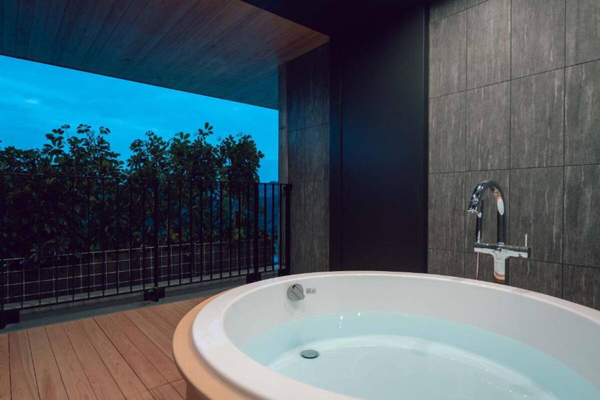A modern outdoor hot tub area with a view of trees and a metal fence.