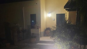 A dimly lit entrance with a pathway leading to a building. There are potted plants and a small light fixture visible. - Lovely attic room (Sant'Agata di Militello)