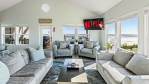 A living room with two grey sofas, a coffee table, and a large TV screen displaying 'NETFLIX'.