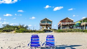 Two beach chairs on a sandy beach with footprints leading to a building with a balcony.