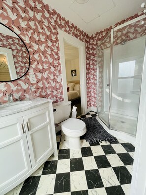 A bathroom with a toilet, sink, and shower. The walls have a bird pattern wallpaper, and the floor has a black and white checkered tile pattern. - Eclectic cottage, steps from downtown (Carlton)