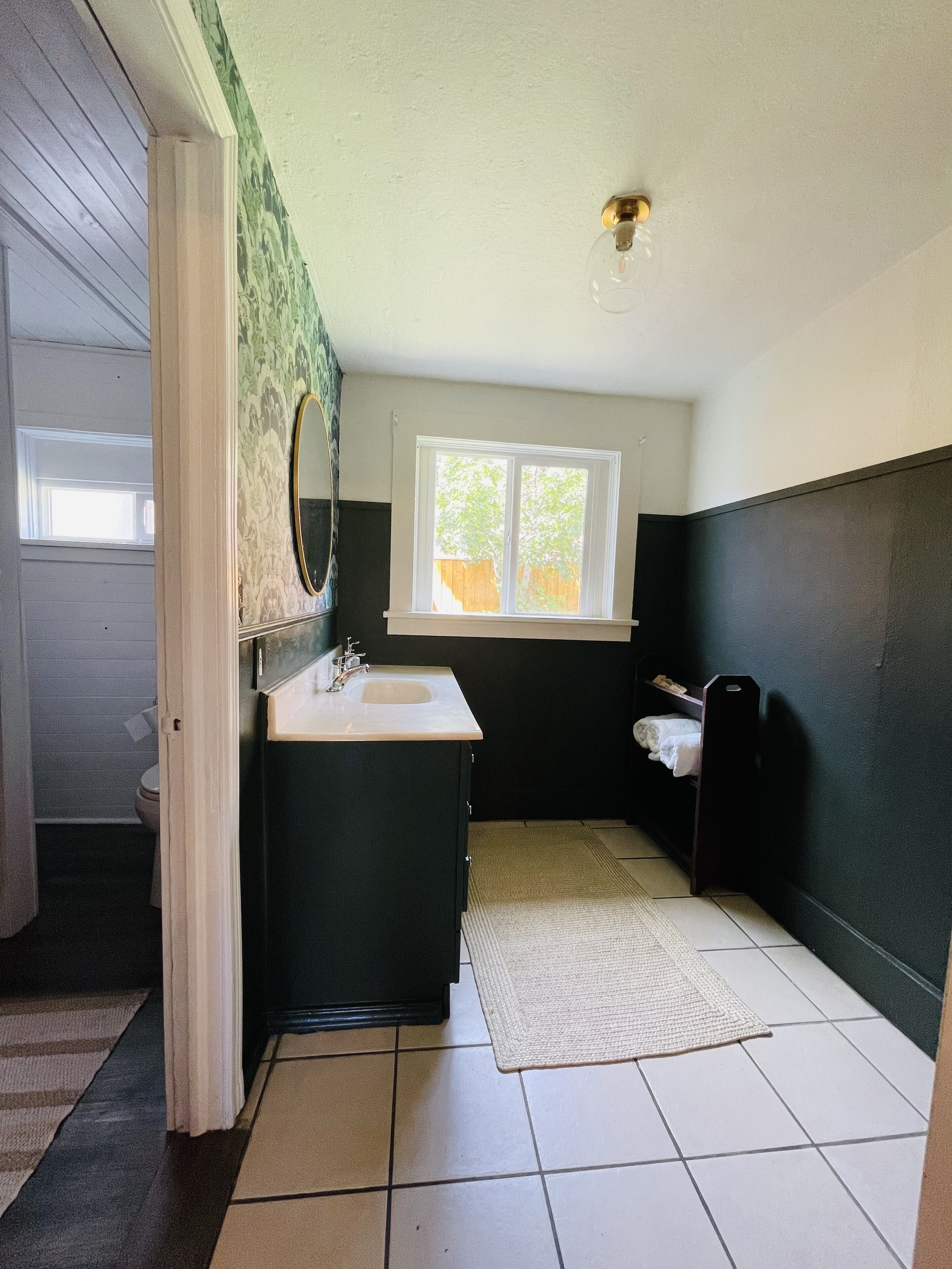 A bathroom with a white sink, dark cabinetry, a window, and a ceiling fan.