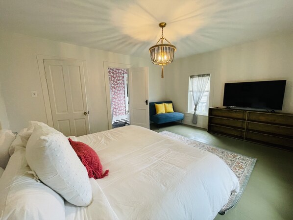 A bedroom with a large bed, a TV, a dresser, and a chandelier. - Eclectic cottage, steps from downtown (Carlton)