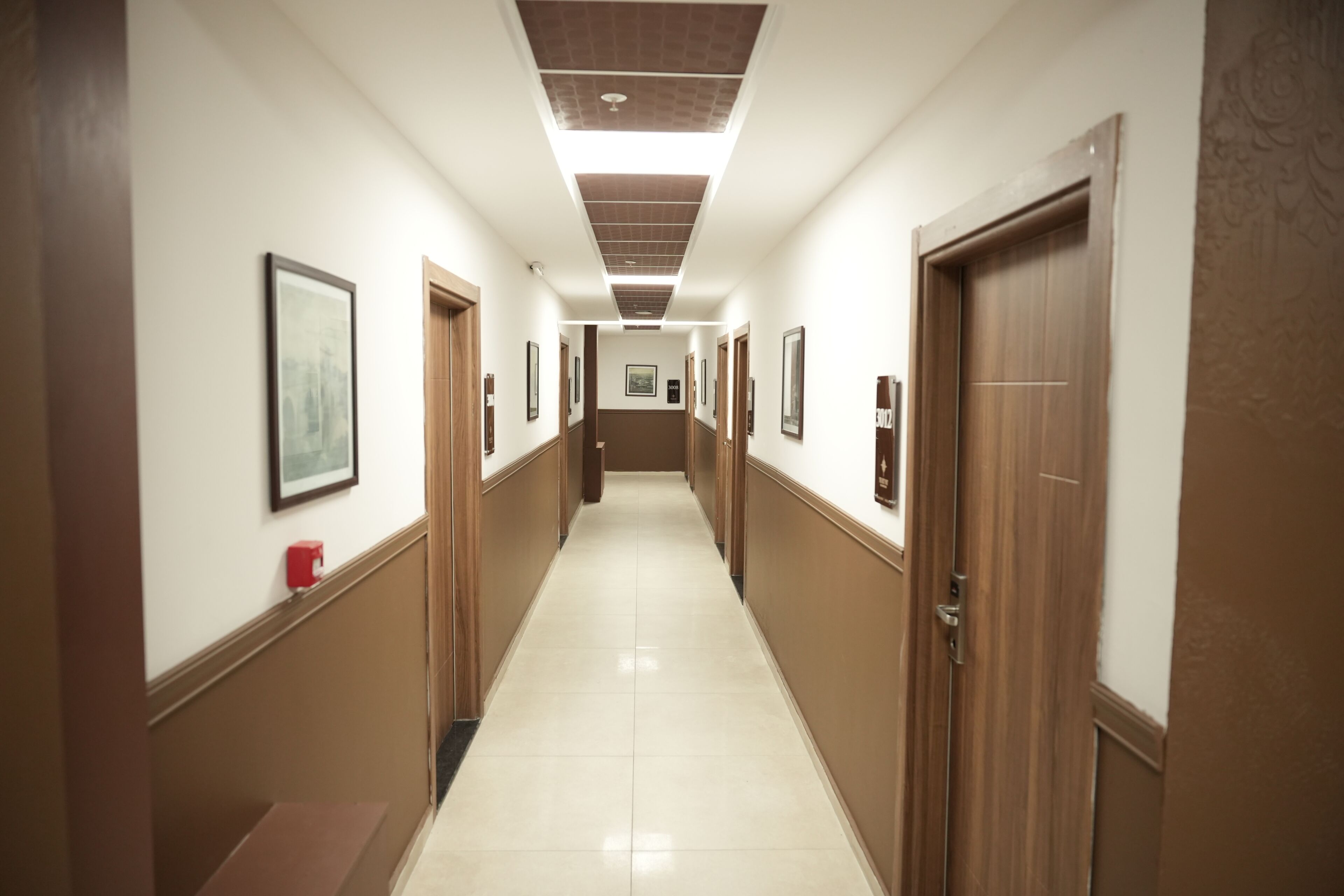 A long, narrow hallway with doors on both sides, a tiled floor, and framed pictures on the walls.