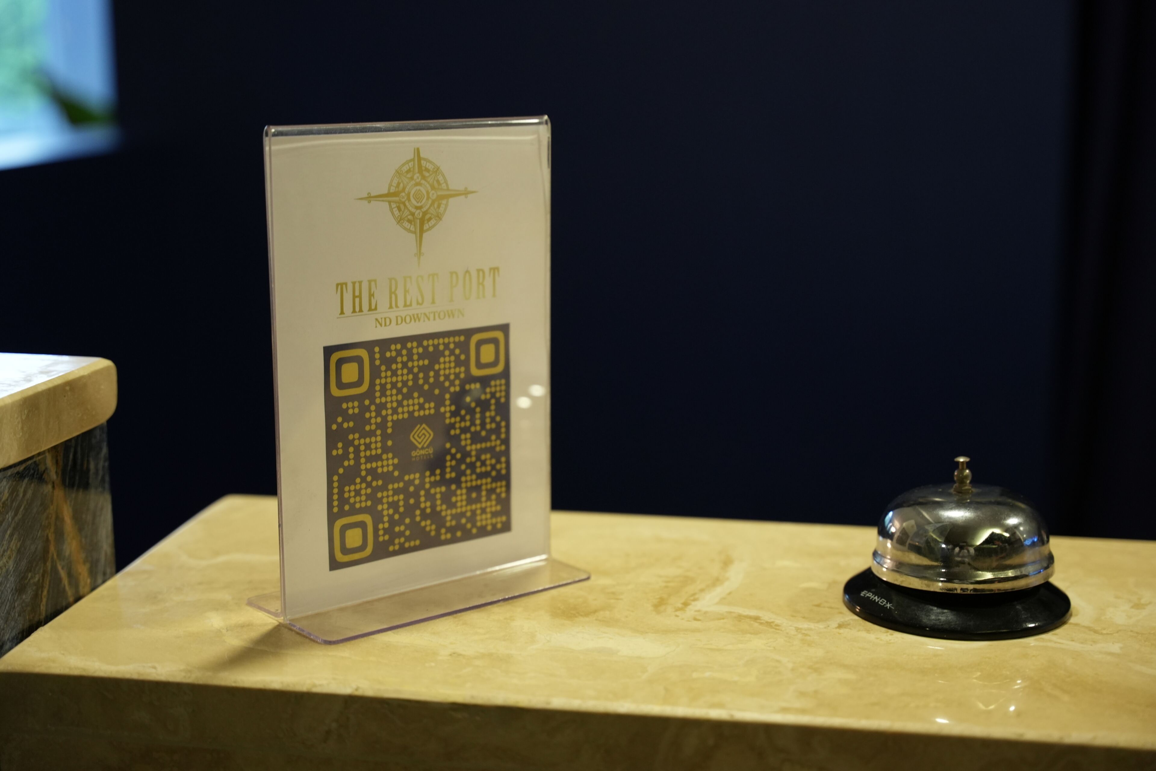 A QR code sign for 'The Rest Port No Downtown' on a marble surface with a bell beside it.