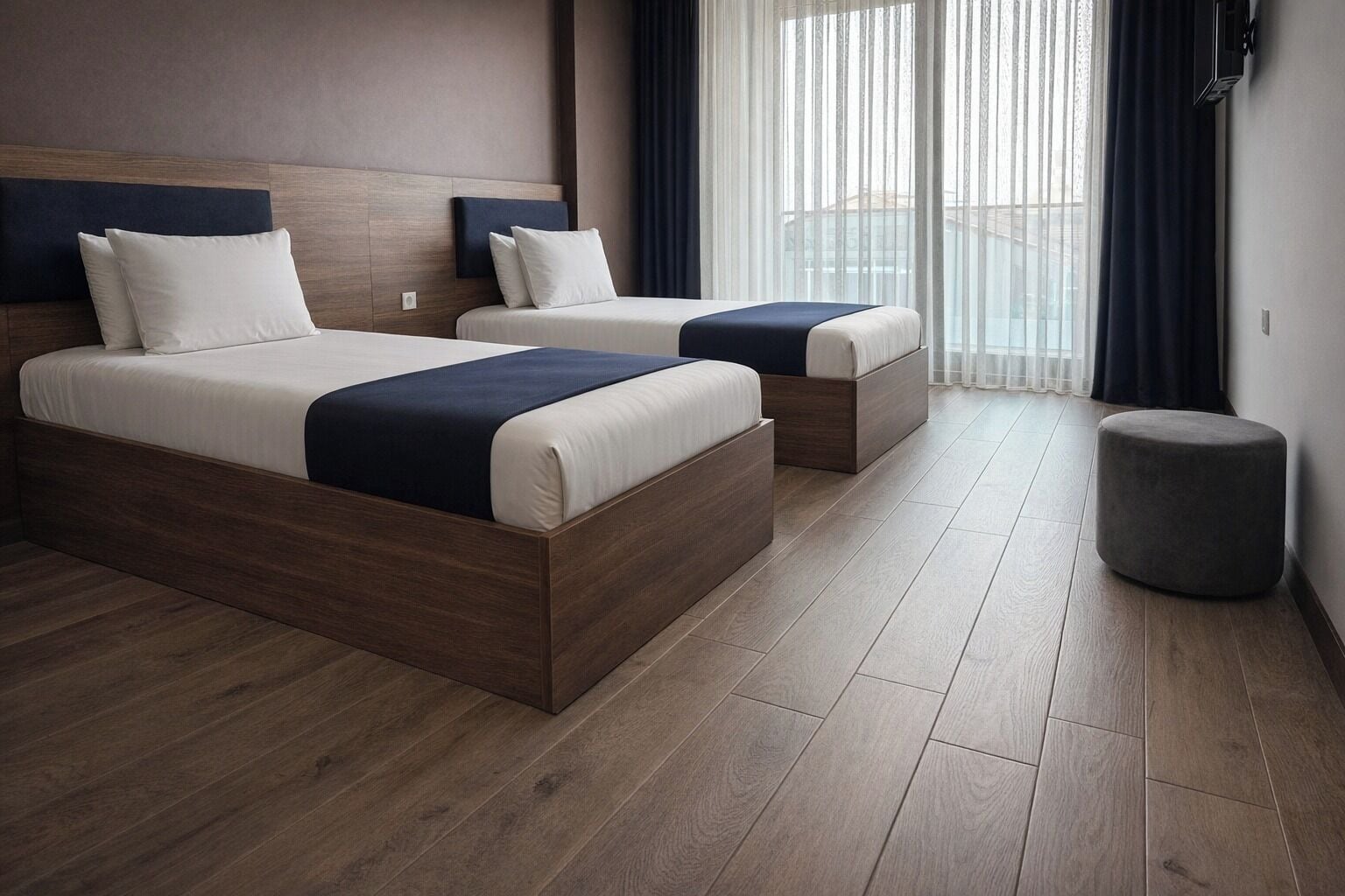 A hotel room with two beds, a small ottoman, and a view of the city through large windows.