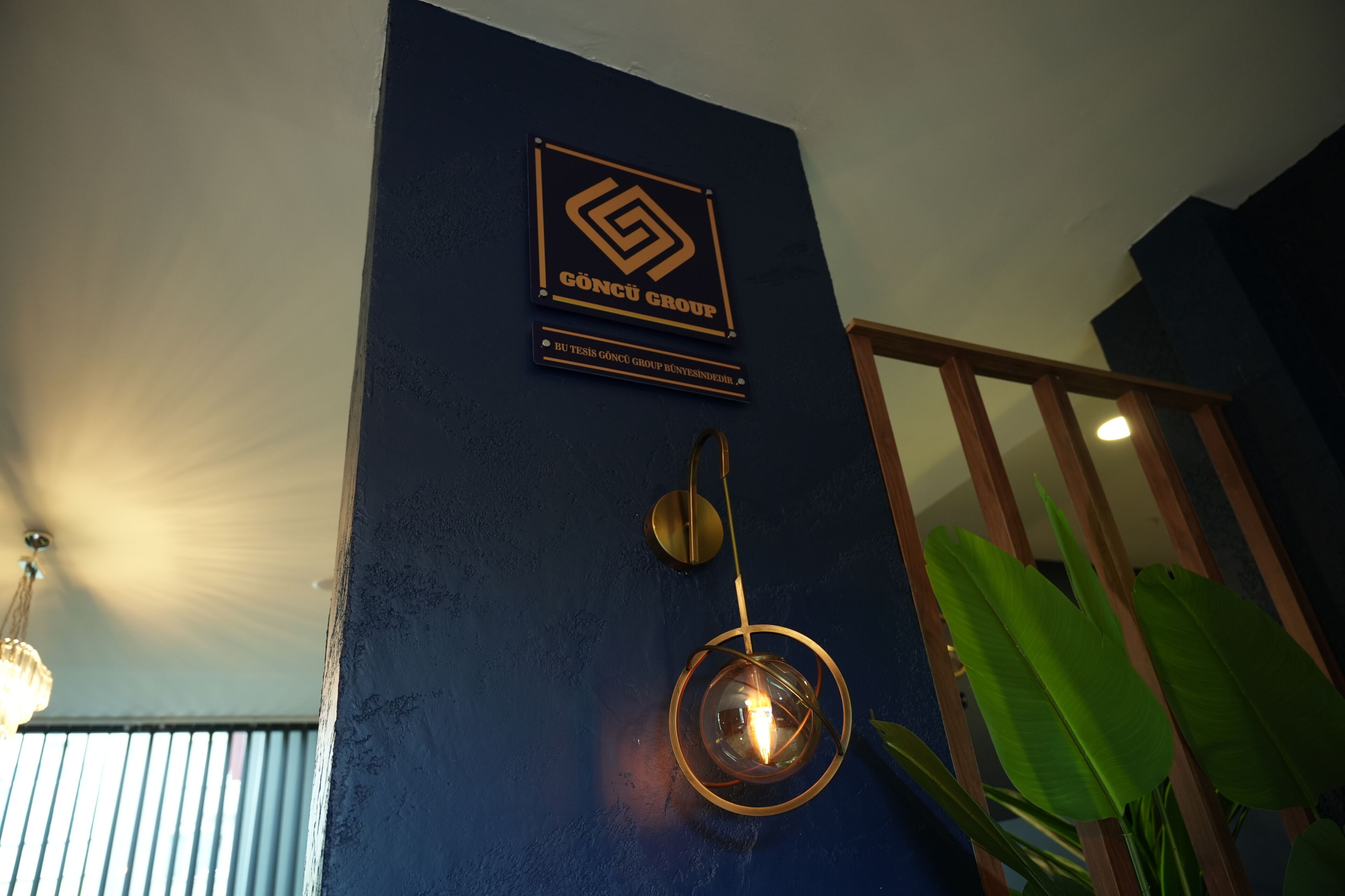 A wall with a logo and text, a hanging light fixture, and a plant.