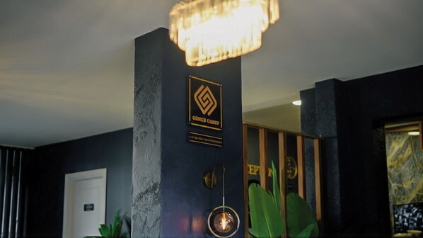 A lobby with a dark wall, a logo plaque, a door, and a plant.