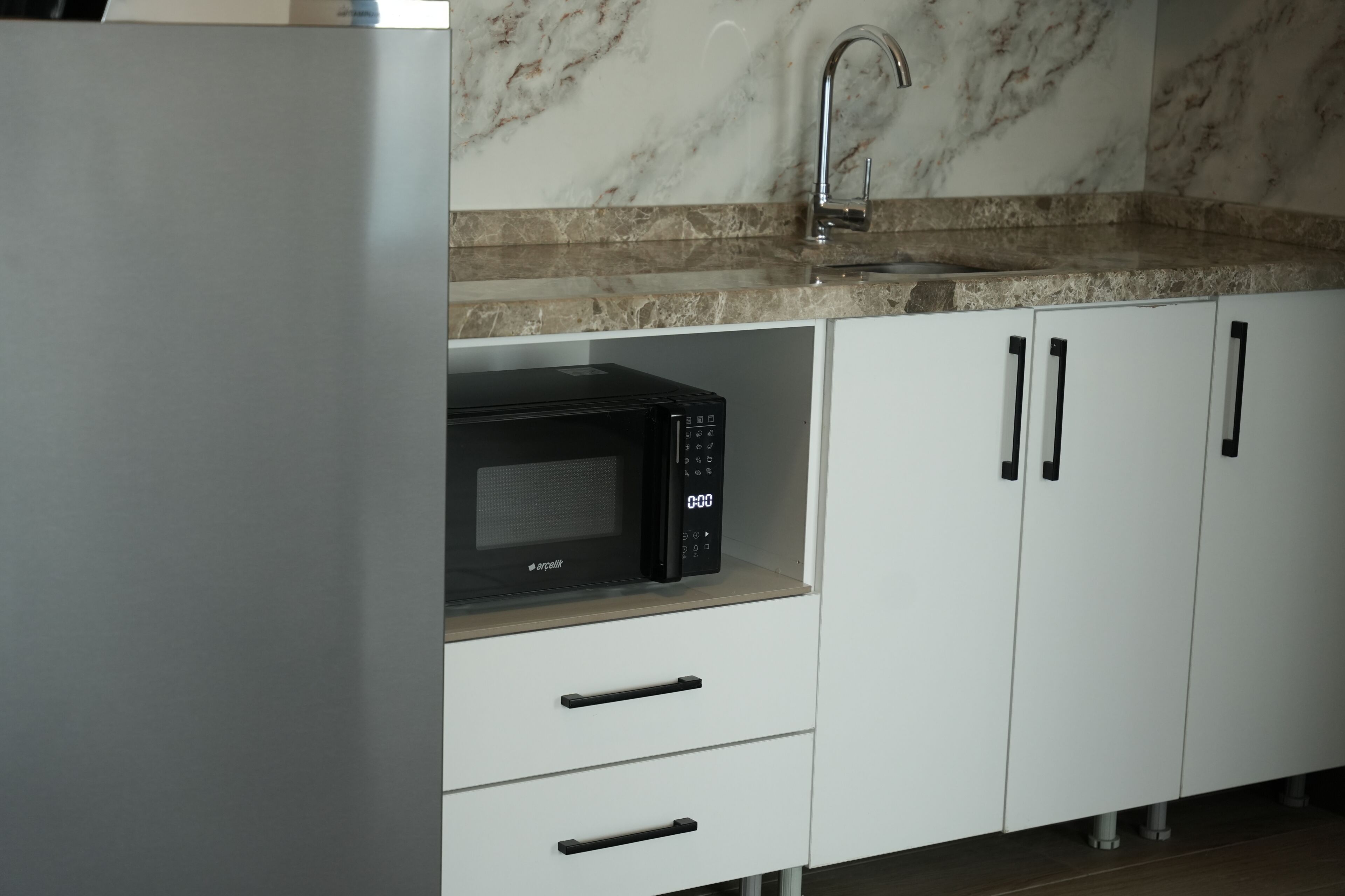 A kitchen with a microwave, a sink, and white cabinets.