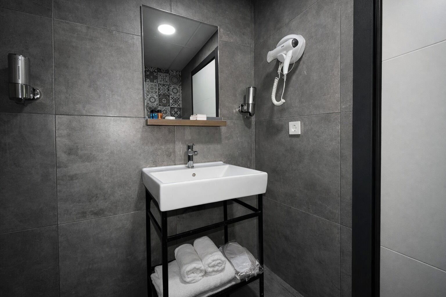 Une salle de bain moderne avec un lavabo blanc, un porte-serviettes, un sèche-cheveux et un miroir.