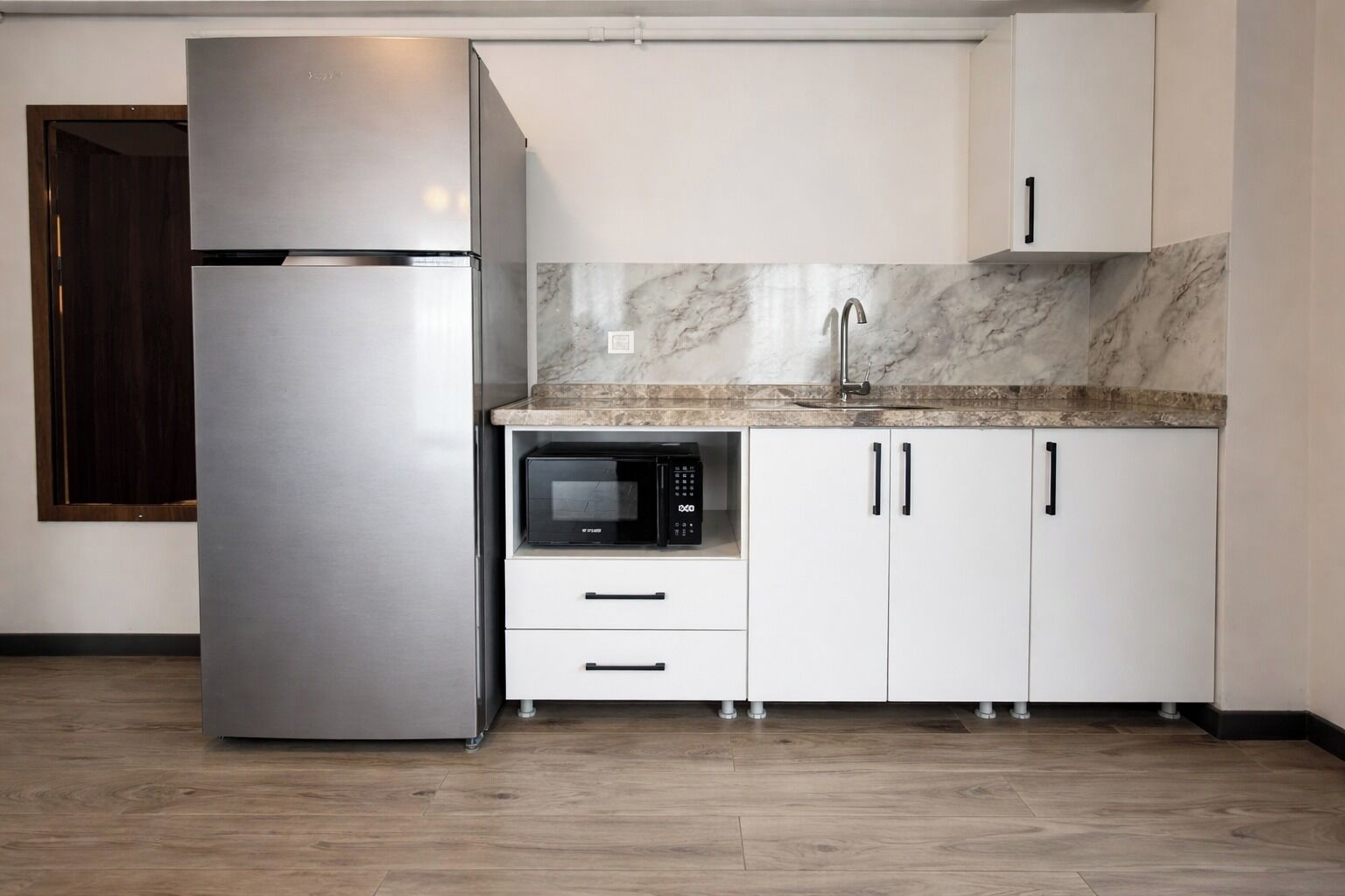 A kitchen with a stainless steel refrigerator, a microwave, white cabinets, and a marble backsplash.