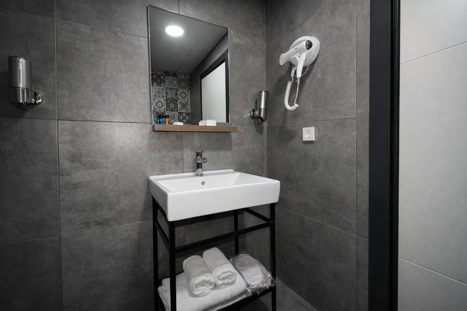 A modern bathroom with a white sink, a towel rack, a hairdryer, and a mirror.