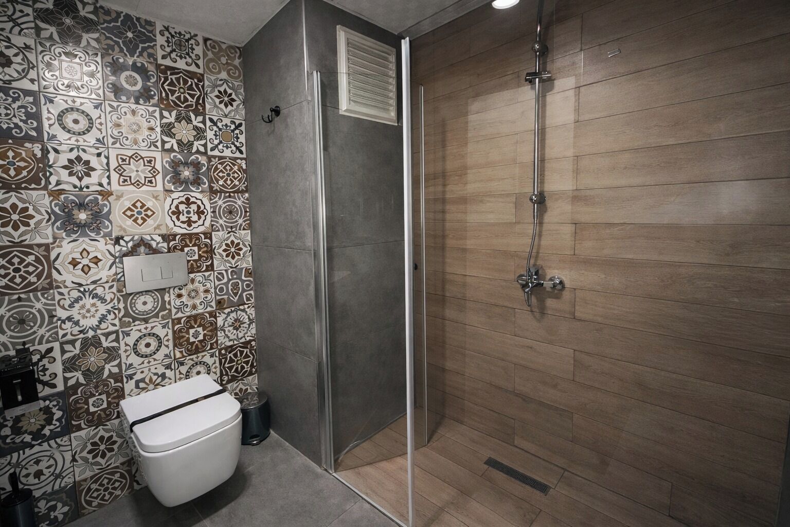 A bathroom with a toilet, shower, and patterned tiles.