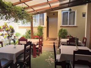 Een terras met tafels en stoelen, overdekt met een houten pergola, omringd door potplanten.