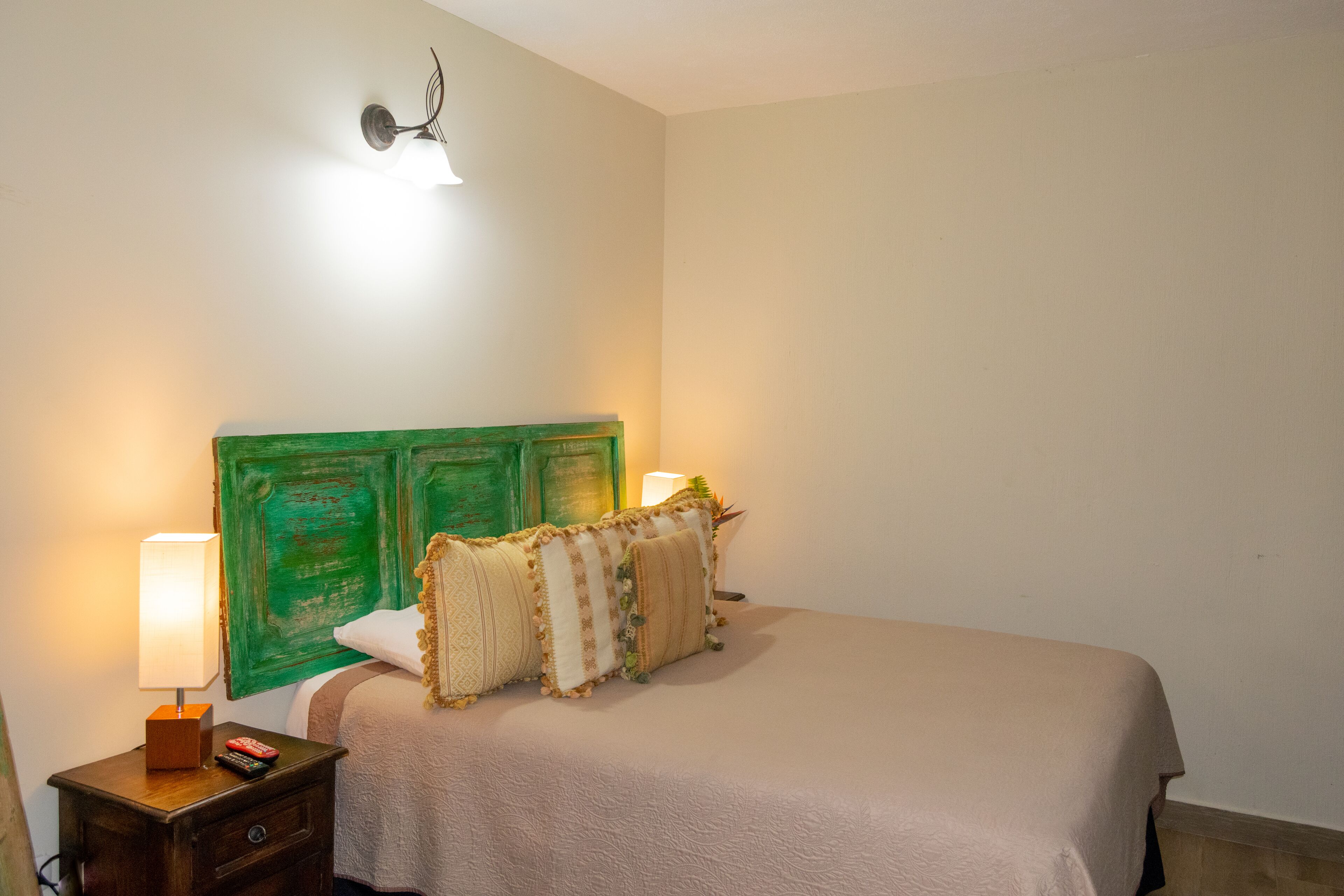 Un lit bien fait, avec une tête de lit verte, une lampe de chevet et une télécommande posée sur une table de chevet en bois.