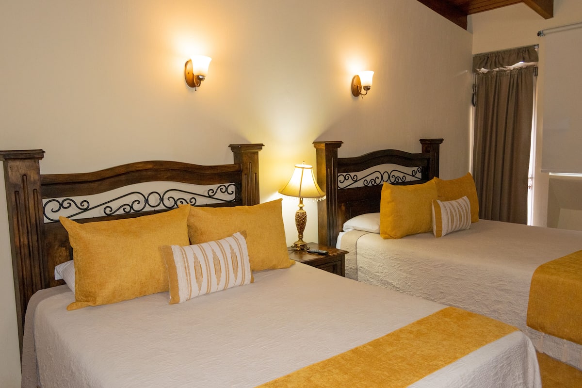 Une chambre d’hôtel avec deux lits, chacun doté d’une tête de lit en bois et d’une couvre-lit blanche. Deux lampes murales sont fixées de part et d’autre des lits.