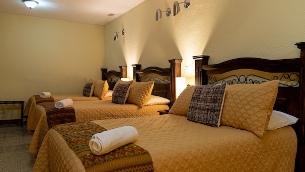 Een hotelkamer met drie bedden, elk voorzien van een gewatteerde spreideken en kussens, en een houten hoofdbord.
