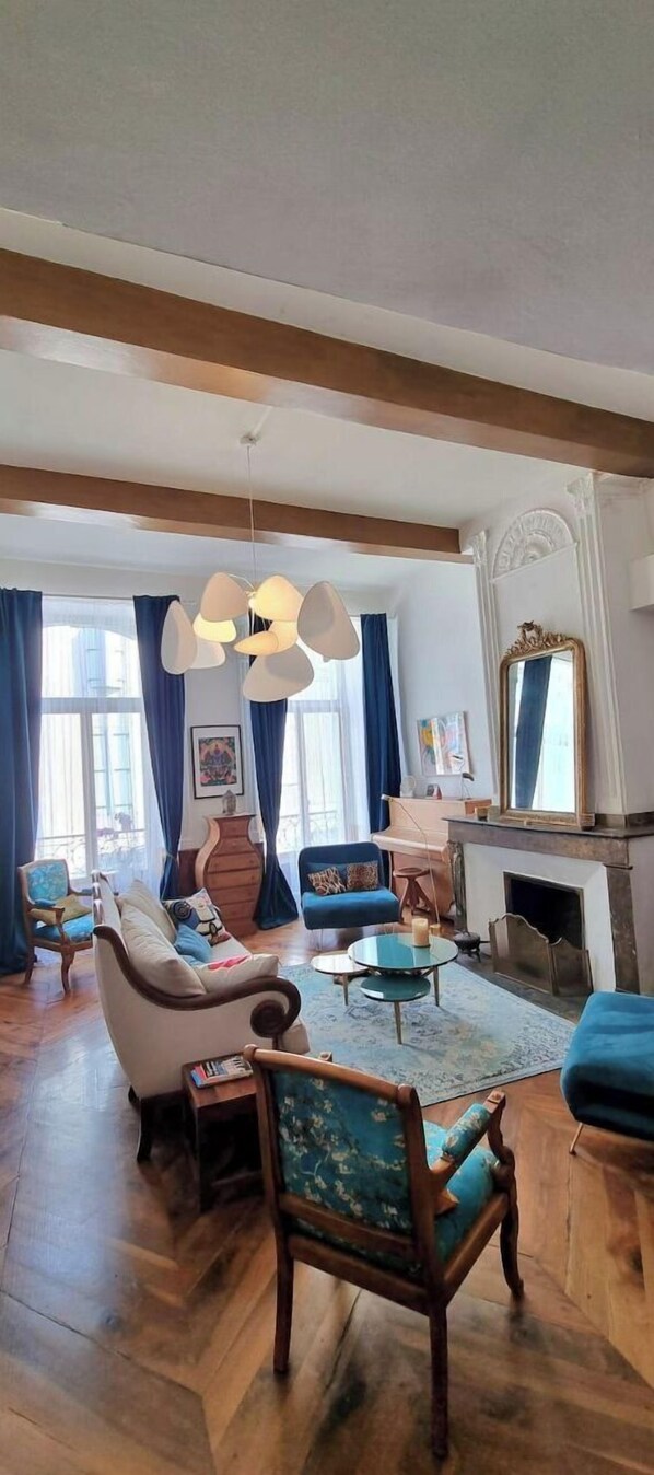 A spacious living room with a fireplace, wooden floors, and a large window with blue curtains.