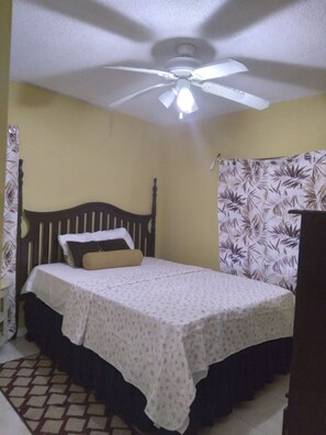 A single bed with a wooden headboard, a ceiling fan, and a patterned curtain.