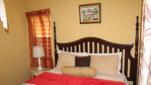 A neatly made bed with a red blanket, a bedside table with a lamp, and a painting on the wall.