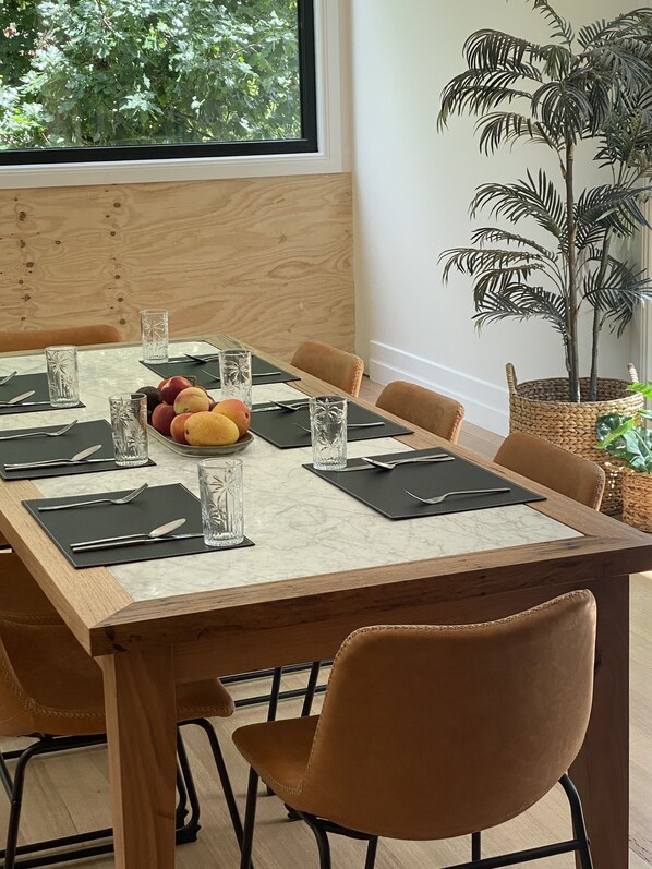 Une table à manger dressée avec des verres transparents, des assiettes de fruits et des sets de table noirs.