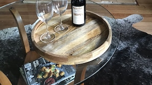 Eine Flasche Delatini-Wein auf einem Holztisch mit zwei Gläsern, vor einem Kamin mit Feuer.
