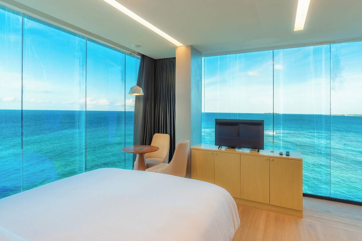 Een hotelkamer met een groot bed, een televisie, een tafeltje en uitzicht op de oceaan.