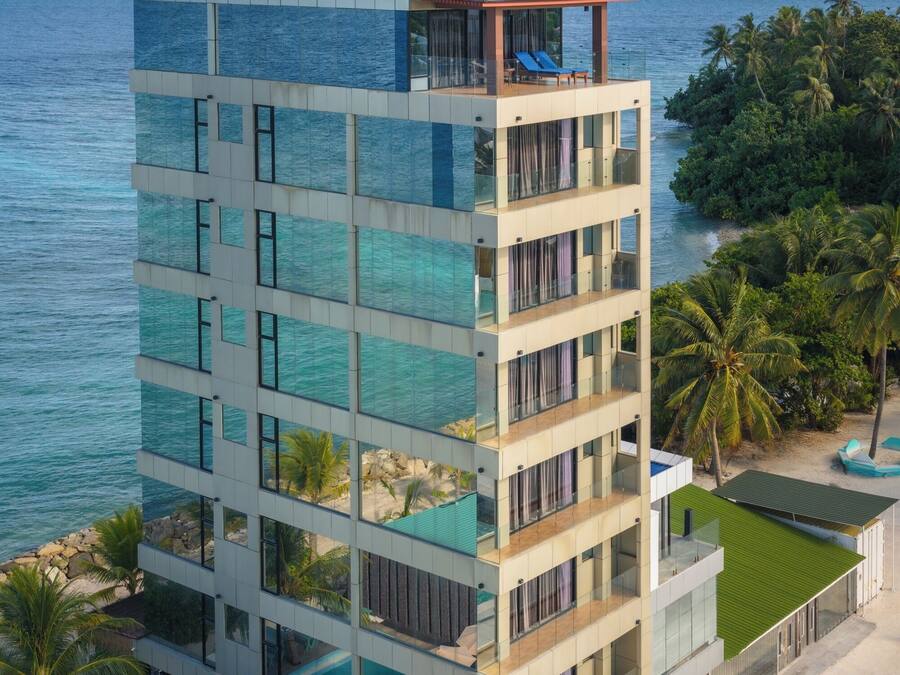 A multi-story hotel with a pool, balconies, and a view of the sea.