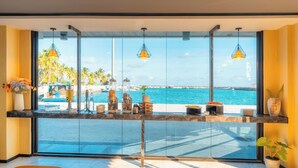 Habitación de hotel moderna con un ventanal grande que da a una piscina y una playa.