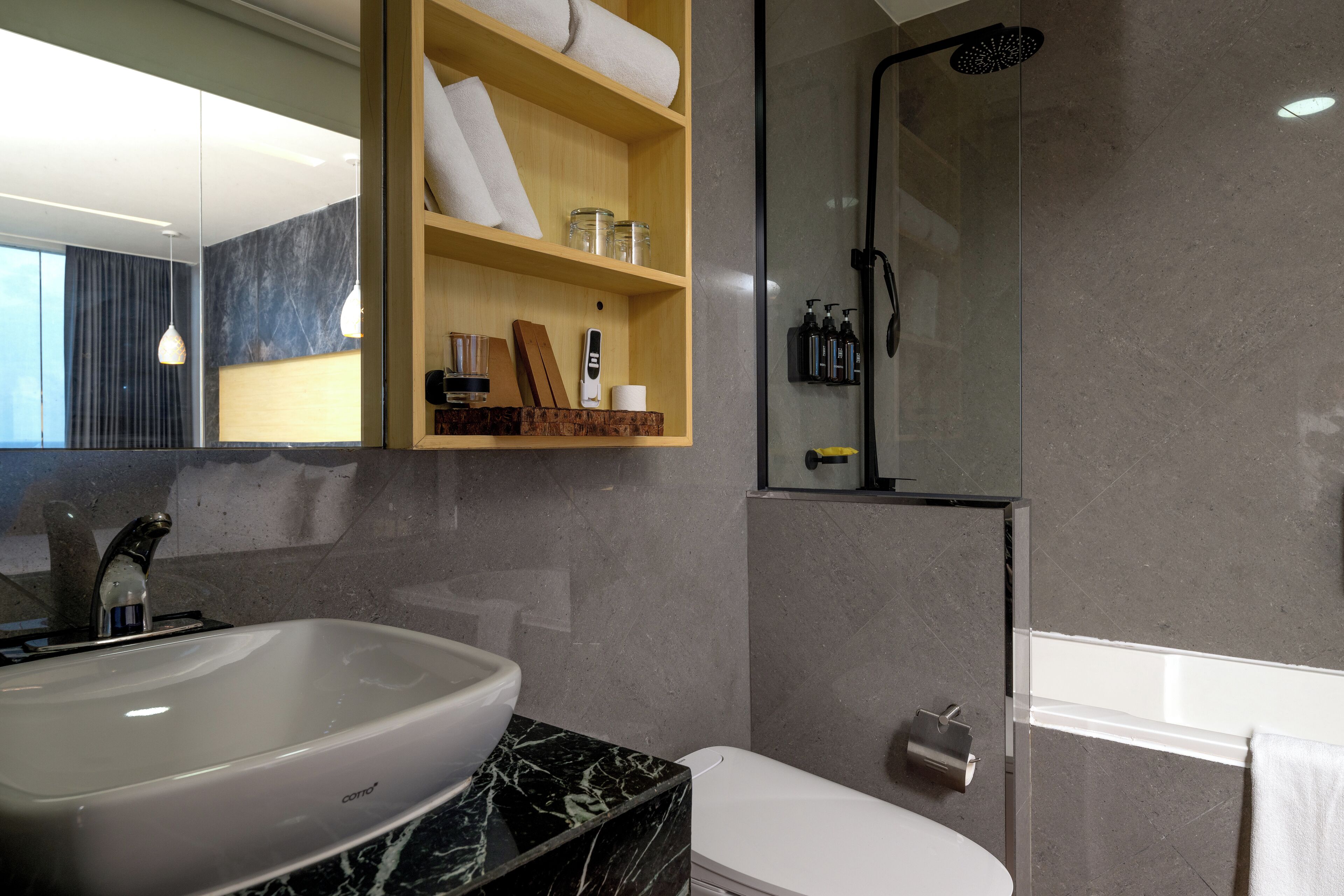 A modern bathroom with a marble sink, a toilet, a glass-enclosed shower, and wooden shelves with toiletries.