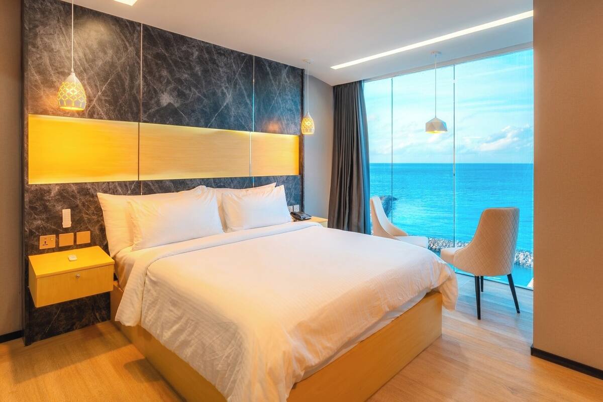 Een hotelkamer met een groot bed, een nachtkastje, een stoel bij het raam en uitzicht op de oceaan.