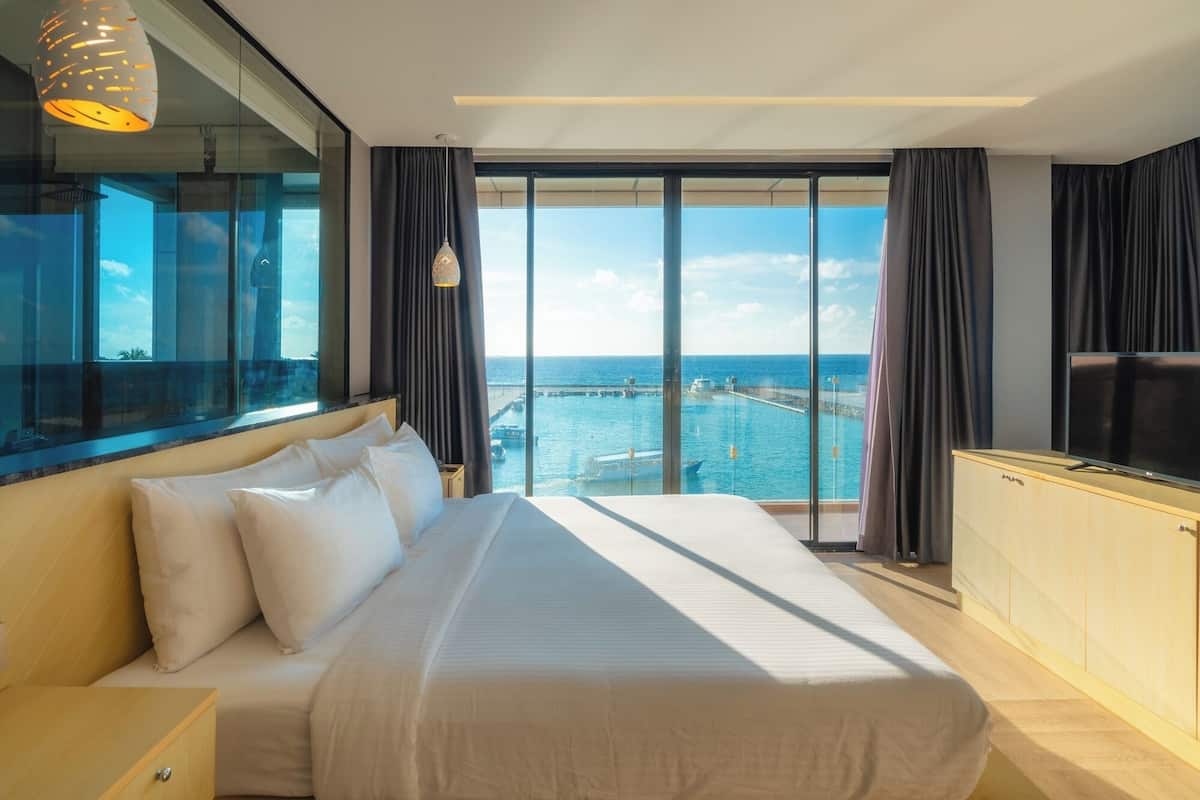 Een moderne hotelkamer met een groot bed, een televisie en uitzicht op zee.