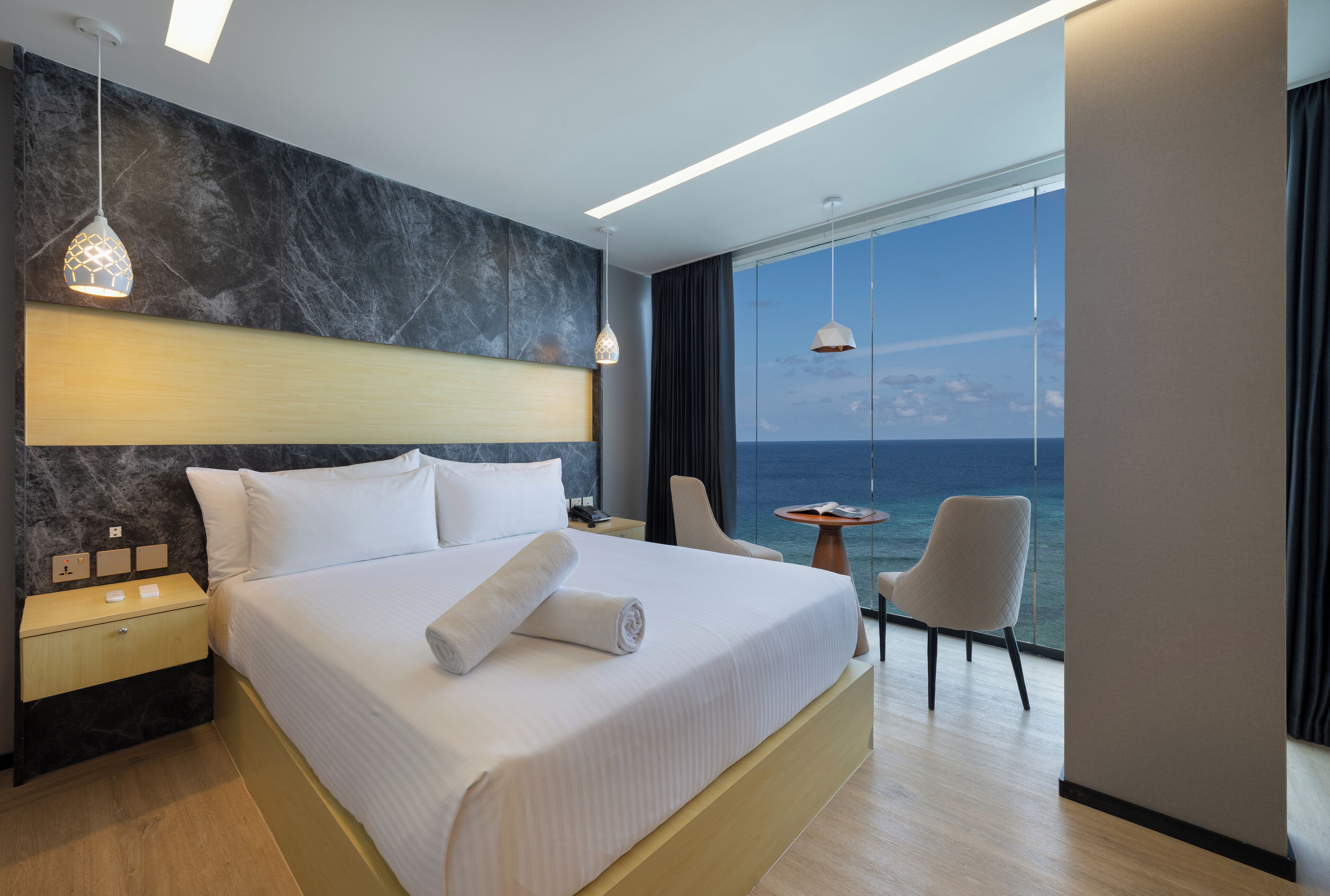 Une chambre d’hôtel moderne avec un grand lit, une table de chevet, une chaise et une vue sur la mer.
